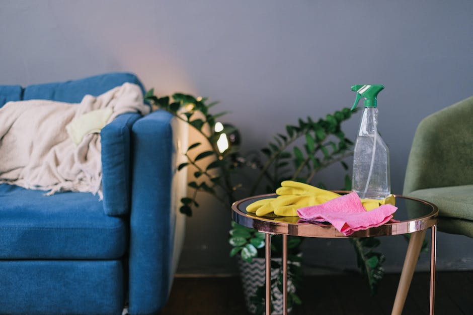 A close-up view of a green upholstered armchair with wooden legs situated in a modern living room. In front of the chair is a round black side table with thin metallic legs, on which there are yellow 